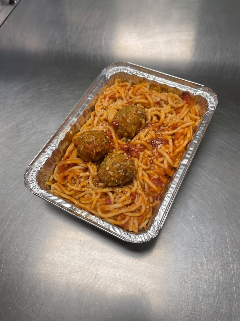 Spaghetti with meatballs and tomato sauce, sprinkled with cheese, in a foil takeout container.